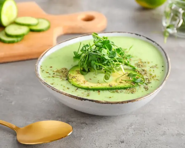 Gazpacho de aguacate cremoso con rodaja de aguacate y brotes verdes, servido en un cuenco blanco.