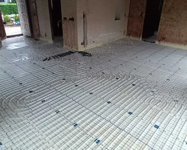 Installation d'un plancher chauffant en cours de renovation. Les tuyaux blancs sont posés sur des panneaux isolants, prêts à être recouverts.