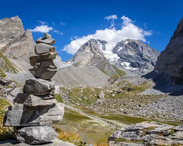 Un cairn, une pile de pierres, marque le chemin dans un paysage de montagne spectaculaire, avec un glacier au loin.