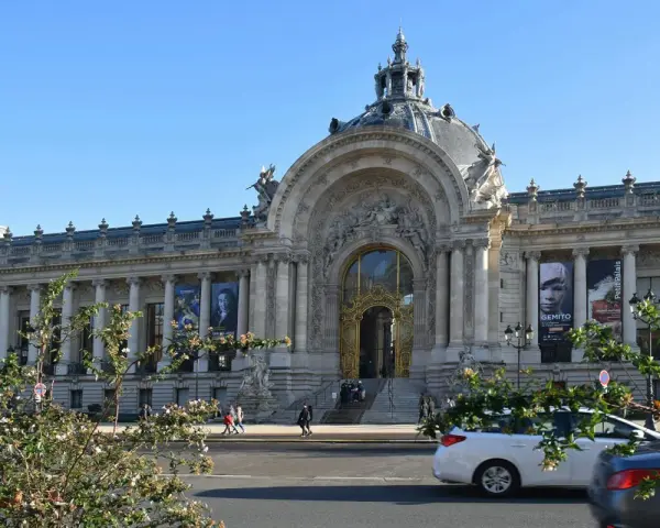 El Petit Palais, un edificio majestuoso con una cúpula y una entrada dorada, exhibe carteles de arte bajo un cielo azul.