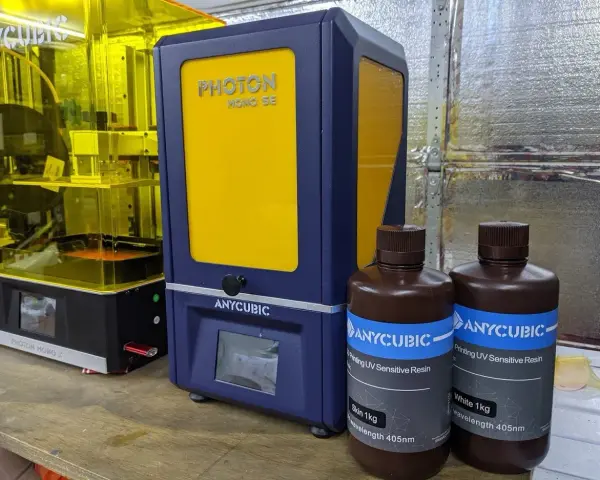Dwa drukarki 3D Anycubic, w tym Anycubic Photon Mono SE, oraz butelki z żywicą do druku.