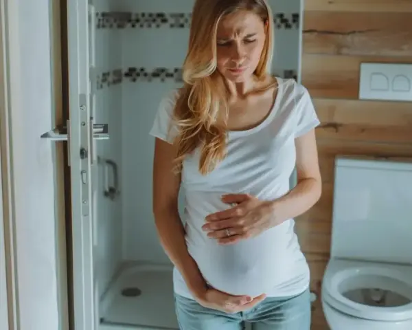 Kobieta w ciąży z wyrazem bólu na twarzy trzyma się za brzuch. Może to być ból podbrzusza w ciąży.
