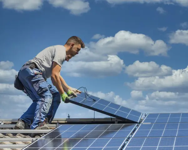 Instalator montuje panele fotowoltaiczne na dachu. Optymalne ustawienie paneli wschód-zachód zapewni maksymalne wykorzystanie energii słonecznej.