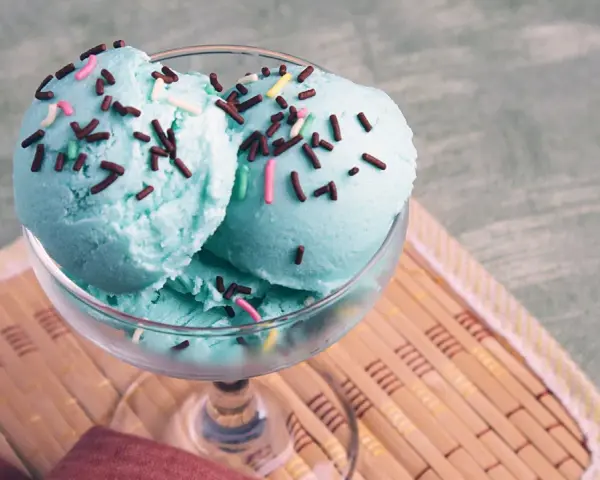Ein Glas mit drei Kugeln blaues Eis, bestreut mit Schokostreuseln und bunten Zuckerstreuseln.