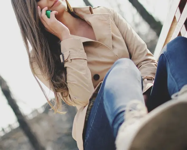 Kobieta w beżowym płaszczu z lumpeksu rozmawia przez telefon, siedząc na ławce. Jak wyczyścić płaszcz z lumpeksu?