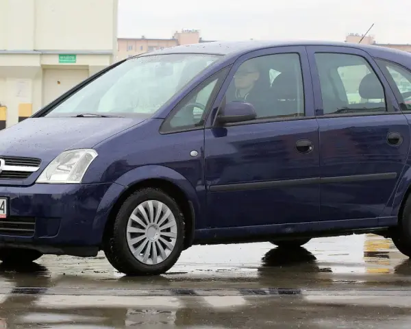 Granatowy Opel Meriva na mokrej nawierzchni. Kierowca w okularach. Wiele pozytywnych opinii o tym modelu.