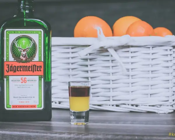 Butelka Jägermeistera i shot z dwoma warstwami, obok koszyk z pomarańczami. Idealne na wieczór, jak pić jagermeister.