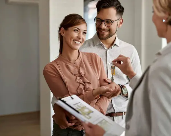 Pareja feliz recibe las llaves de su nuevo hogar, con un agente inmobiliario mostrando las escrituras de una casa.