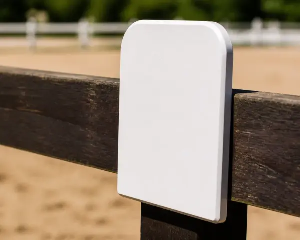 Un panneau blanc vierge sur une clôture en bois dans une carrière de dressage.