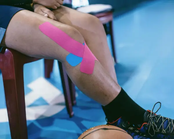 Sportowiec z plastrami na kolanie, przygotowujący się do ćwiczeń na chondromalację rzepki.