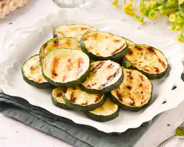 Rodajas de calabacín a la plancha, tiernas y con marcas de parrilla, servidas en un plato blanco.