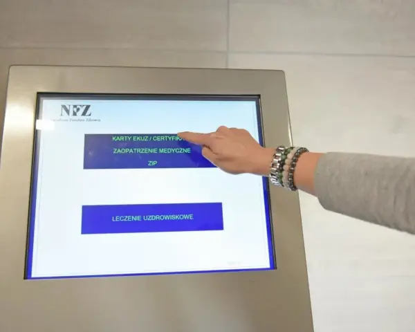 Dłoń dotyka ekranu automatu NFZ, wybierając opcję "Karty EKUZ / Certyfikaty".