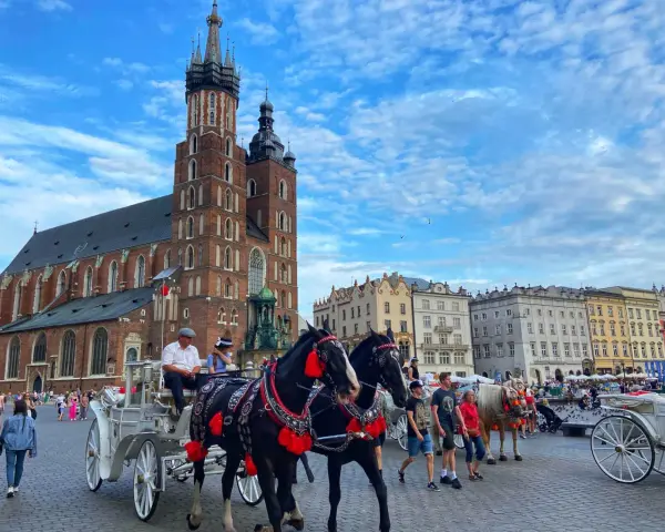 Horse-drawn carriages await tourists in Krakow's Old Town, a picturesque scene from a Poland trip, with St. Mary's Basilica towering in the background.