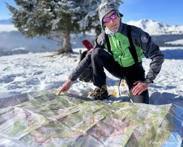 Un homme en tenue de ski pointe une carte sur la neige, planifiant son ascension vers le plus haut sommet de France.