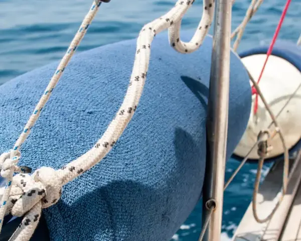 Blauer Fender am Boot befestigen mit Seilen. Das Boot gleitet auf dem blauen Meer.