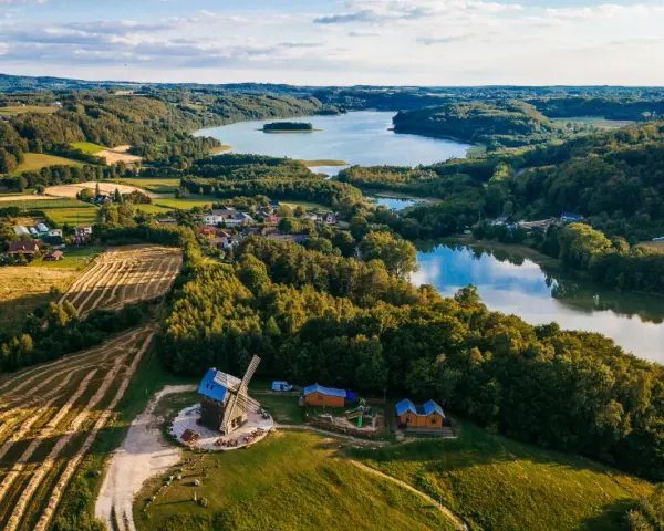 Malowniczy krajobraz kaszub z jeziorem, lasami, polami i drewnianym wiatrakiem.