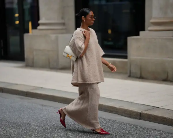 Donna con completo beige e borsa bianca, indossa scarpe rosse con tacco kitten, un dettaglio che aggiunge eleganza.