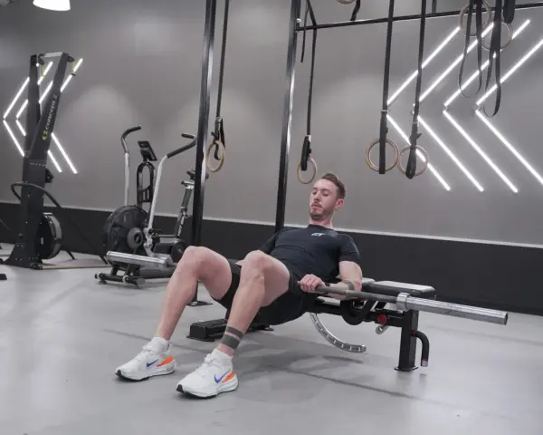 Man utför hip thrust med skivstång på en bänk i ett modernt gym.