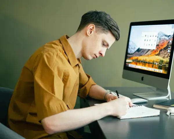 Student pracuje zdalnie, notując pomysły na komputerze. Idealna praca online dla studenta.