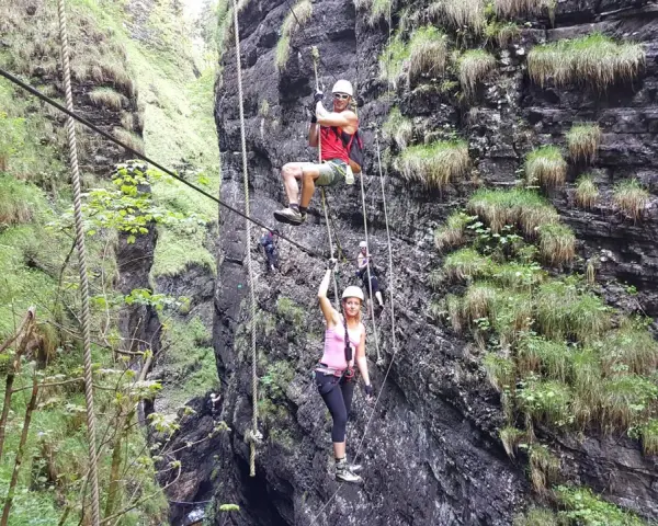 Abenteuer im **Postalmklamm Klettersteig**: Menschen seilen sich durch eine enge Schlucht ab, gesichert an Seilen, umgeben von steilen, bewachsenen Felswänden.