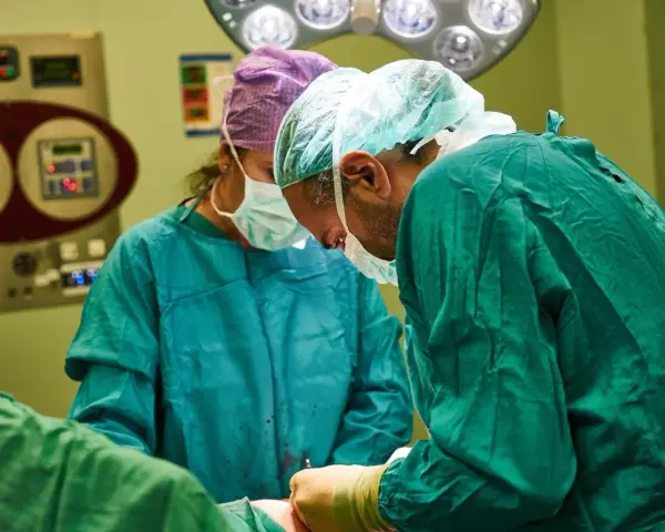 Chirurdzy w maseczkach i czepkach przygotowują się do operacji. Narkoza już działa, pacjent jest bezpieczny.