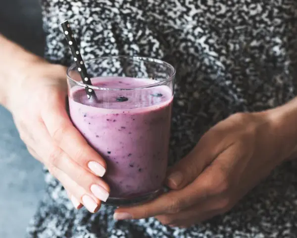Ręce trzymają szklankę z fioletowym smoothie, które może być skuteczną miksturą na zaparcia.