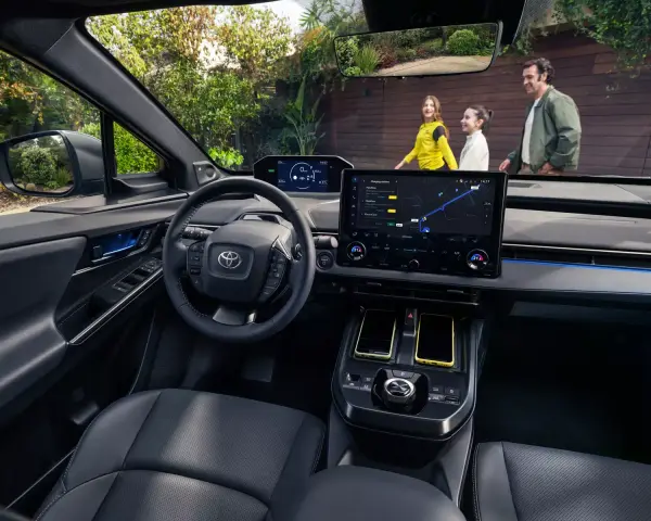 Wnętrze Toyoty bZ4X z ekranem nawigacji. Rodzina na zewnątrz, zastanawia się nad ceną i możliwościami tego elektrycznego SUV-a.