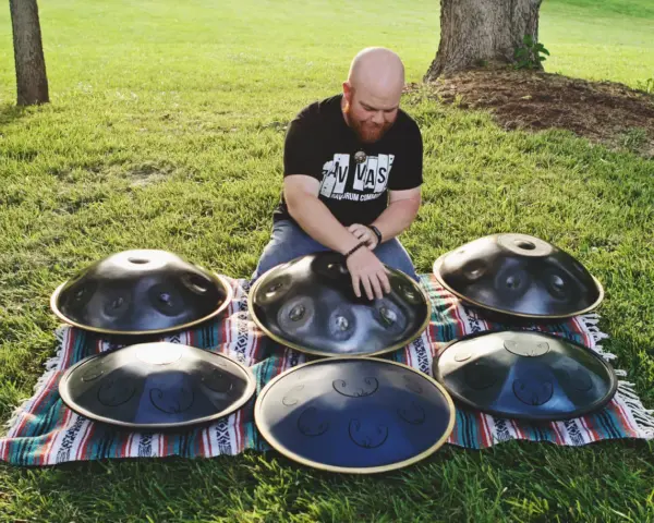 Mann spielt auf mehreren runden Metallinstrumenten im Freien.
