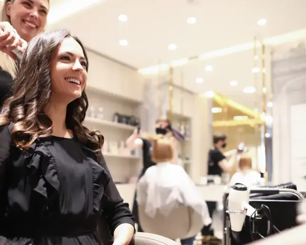 Friseurin stylt lächelnde Kundin mit Lockenstab in modernem Salon.