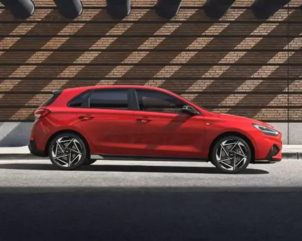 Czerwony Hyundai i30 stoi na tle ceglanej ściany z ciekawymi cieniami.