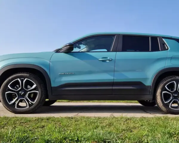 Turkusowy Jeep Avenger 4x4 z czarnymi felgami na tle nieba i trawy.