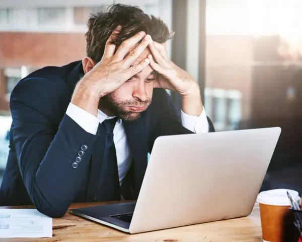 Zestresowany mężczyzna w garniturze z rękami na głowie, patrzący na laptopa. Trudna spłata długu po ogłoszeniu upadłości.
