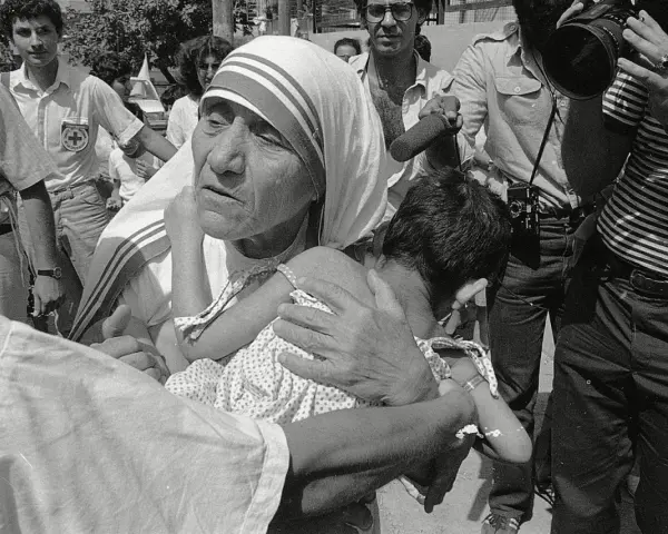 Missionaries of Charity founder, Mother Teresa, cradles a child amidst a crowd and media attention.
