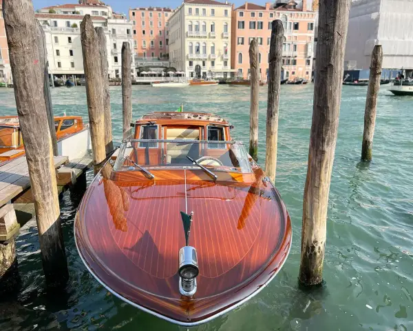 Un elegante taxi boat in legno lucido attende sul Canal Grande a Venezia, pronto a trasportare passeggeri tra i palazzi storici.