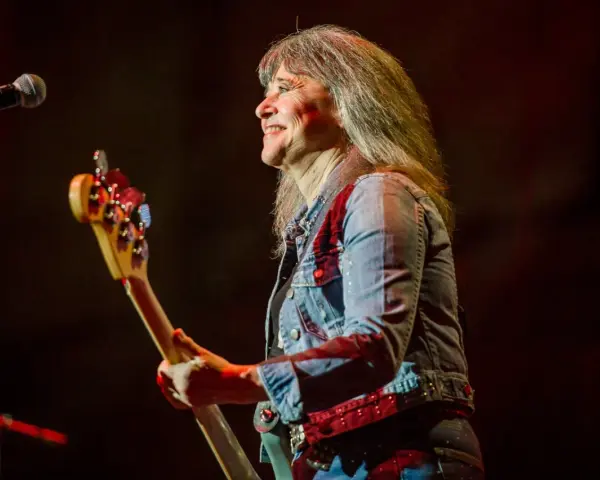 Suzi Quatro dzisiaj na scenie, z basem w ręku, uśmiecha się do publiczności. Rock'n'rollowa legenda w dżinsowej kurtce.