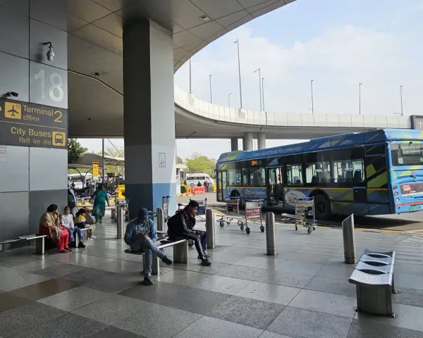 Oczekujący na autobusy na lotnisku Delhi. W tle niebieski autobus elektryczny.