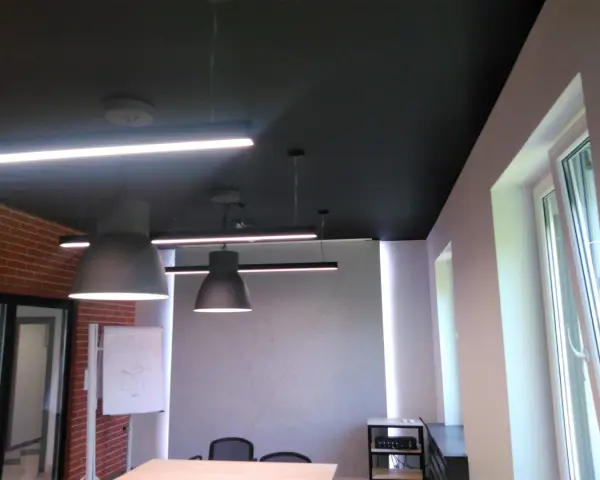 Nowoczesne biuro z czarnym sufitem (RAL 9004), wiszącymi lampami i ceglaną ścianą.