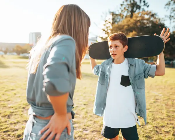 Ein Junge mit einem Skateboard über der Schulter spricht mit einer Frau. Die **Adoleszenz** ist eine spannende Zeit voller Entdeckungen.