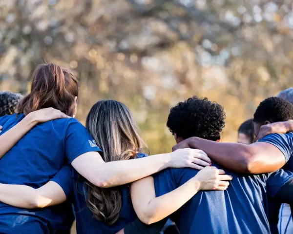 A diverse group of people in blue shirts huddle together, arms around each other, symbolizing collaboration and the strength of revenue diversification.