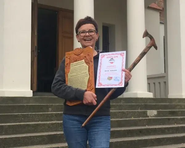 Uśmiechnięta kobieta z dyplomem i drewnianą laską, zdobywczyni Korony Gór Polskich.