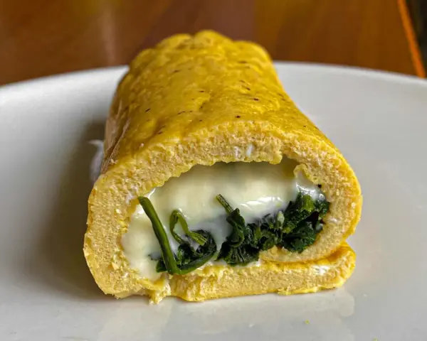Rotolo di frittata dorato, ripieno di spinaci e formaggio filante, servito su un piatto bianco.
