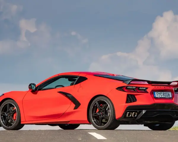 Czerwony Chevrolet Corvette C8 z czarnym spoilerem i felgami, zaparkowany na drodze pod błękitnym niebem z chmurami.