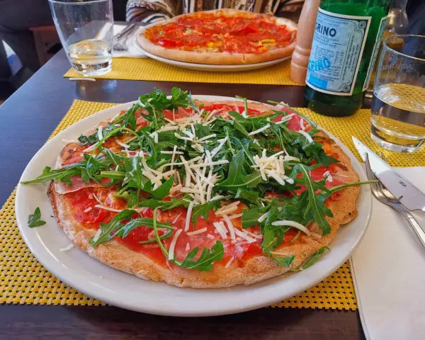 Leckere Pizza mit Rucola und Schinken auf einem Teller, ein Beispiel für glutenfreie Restaurants.