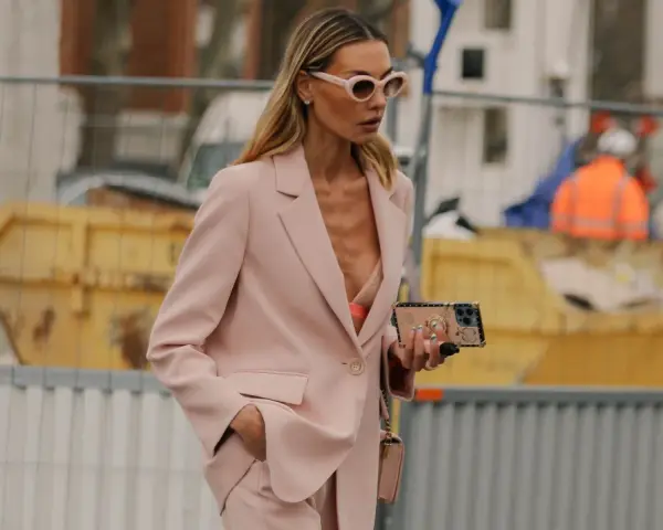 Donna con tailleur rosa, reggiseno a vista e occhiali da sole. Un look chic per ogni occasione.