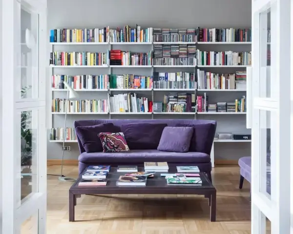 Un divano viola accogliente davanti a una libreria bassa piena di libri e CD.