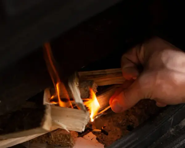 Main allumant un feu dans un poêle à bois avec une allumette.