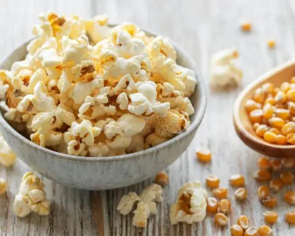 Schüssel mit frisch zubereitetem Popcorn im Topf, daneben eine Holzschaufel voller Maiskörner.
