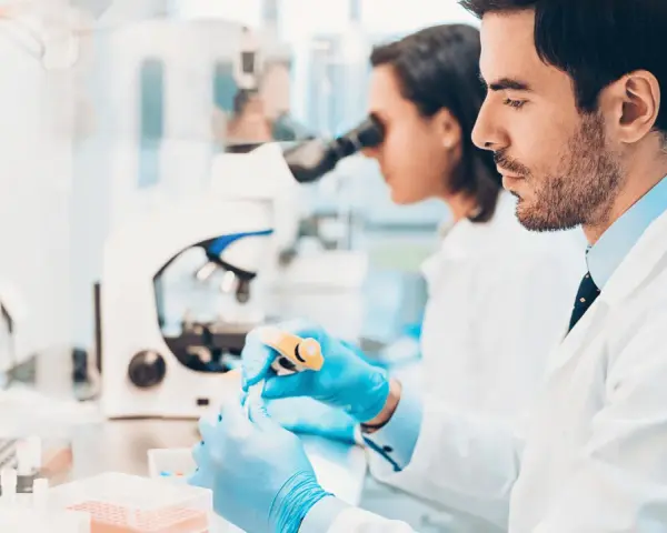 Ricerca di offerte di lavoro tecnico di laboratorio biomedico: due scienziati lavorano con provette e microscopio in un laboratorio moderno.