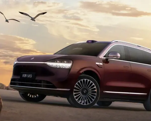 Ciemnoczerwony SUV Aito M9 na tle zachodzącego słońca, z ptakami w locie.