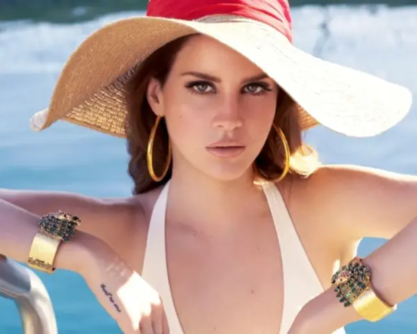 Lana Del Rey, wokalistka, w letnim kapeluszu i biżuterii, relaksuje się przy basenie.